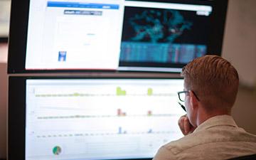 Man looking at computer monitors from a cybersecurity operations center